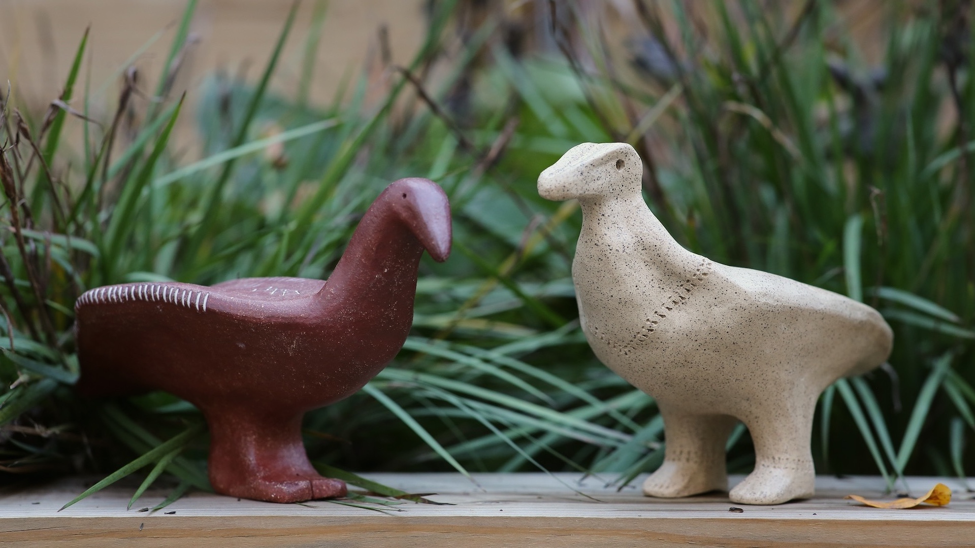 Two abstract bird shapes with human feet. One is made of red clay and one of white clay.